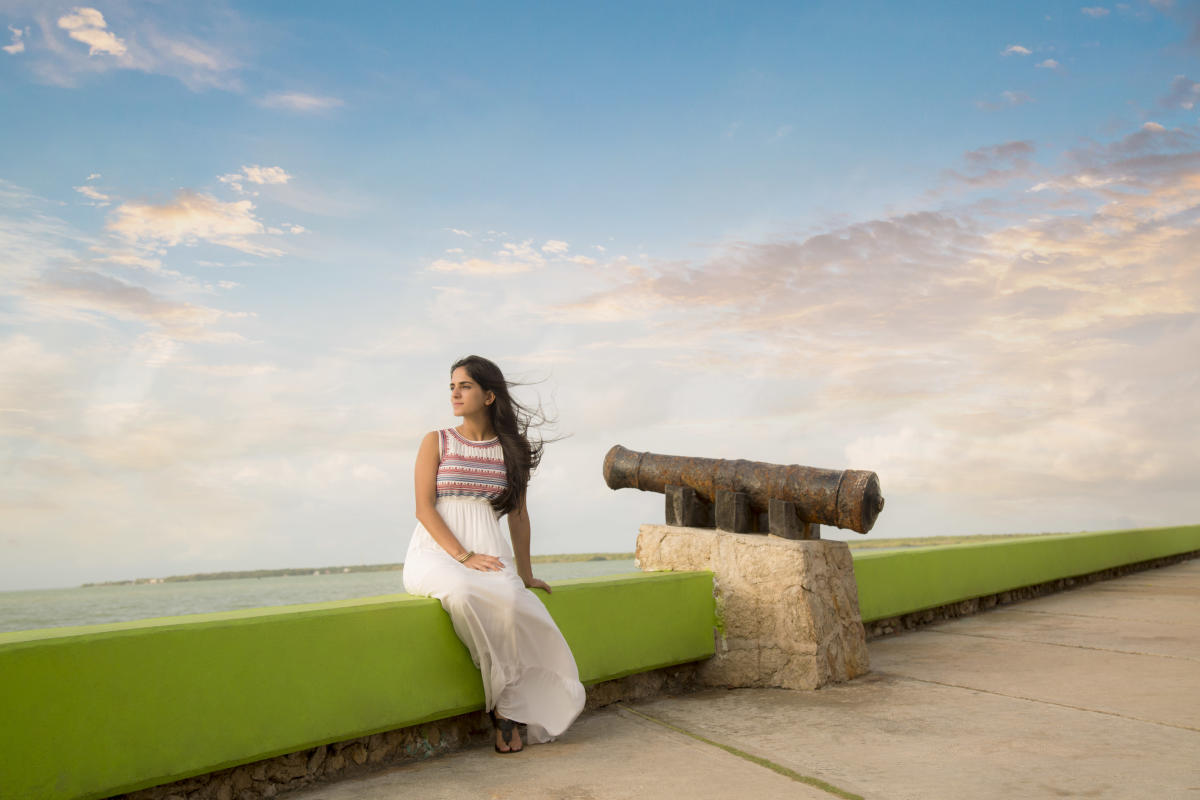 Woman In White Dress Sitting Next To A Cannon Overlooking The Coast In Chetumal