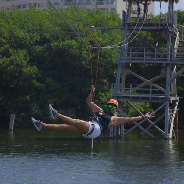 A woman riding on a zipline over the water.