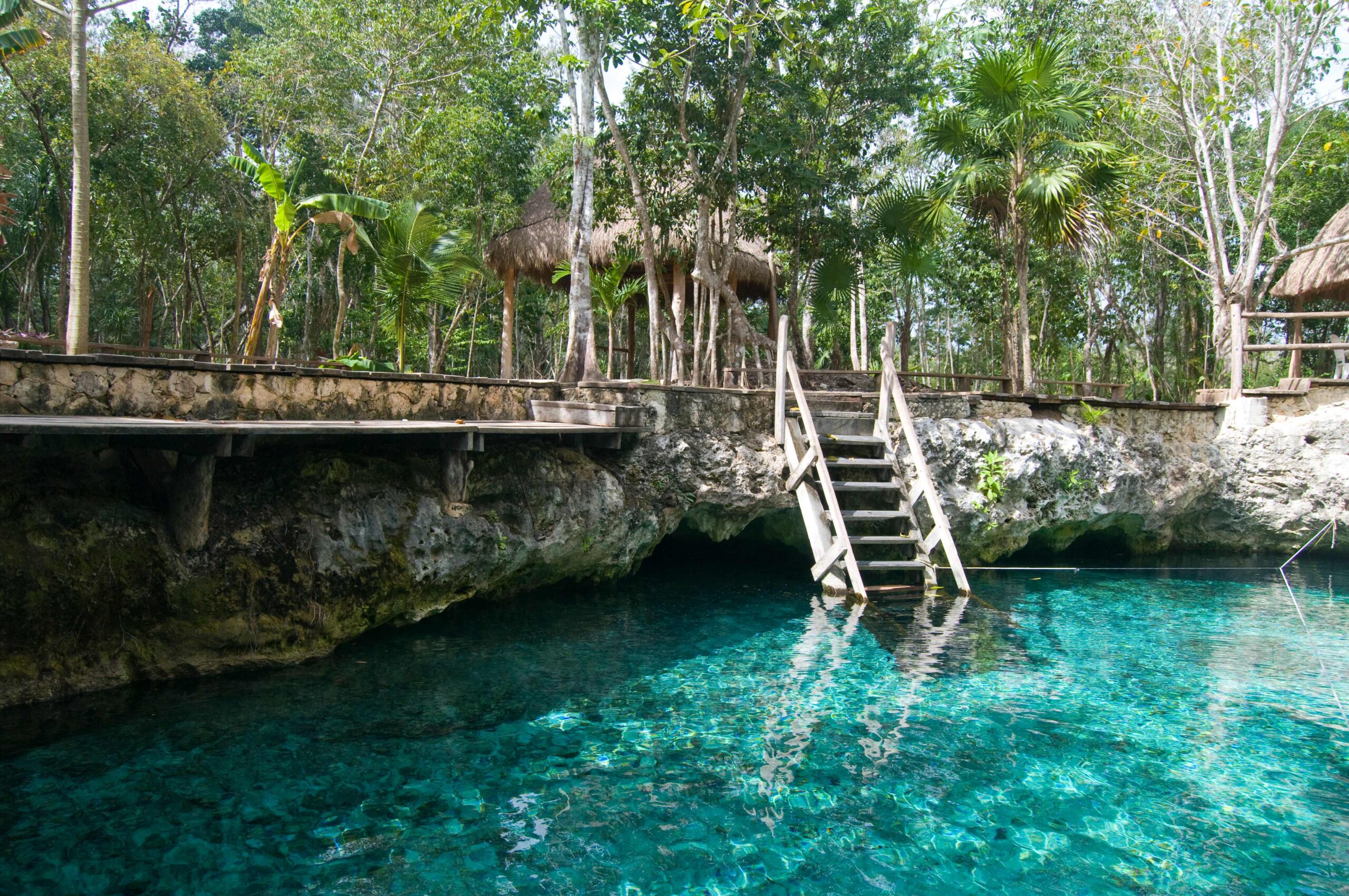 Turquoise cenote with a wooden stairway near Tulum